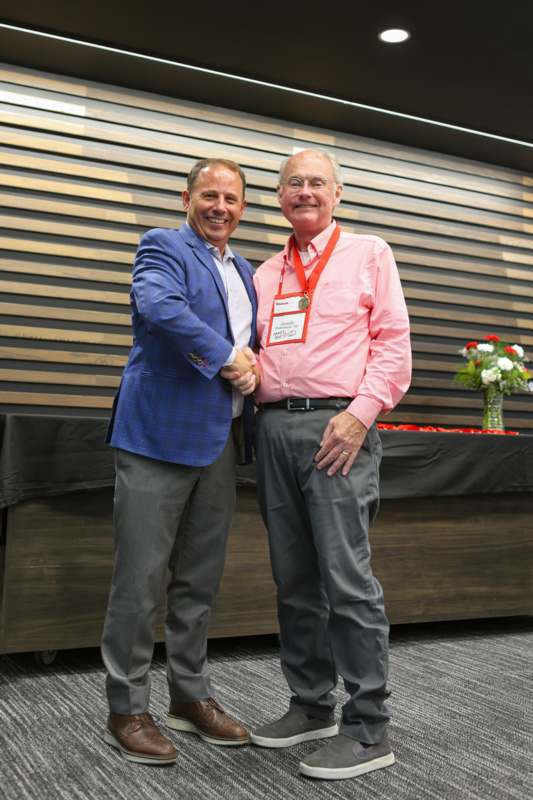 two men shaking hands in front of a wood wall