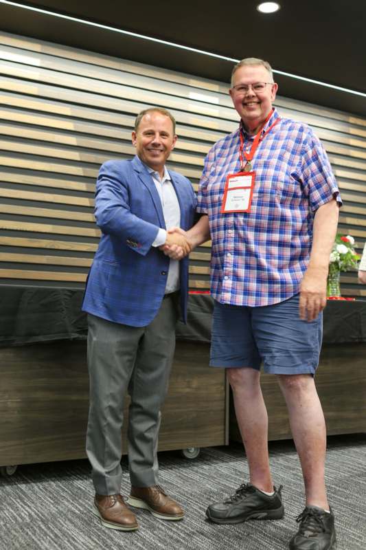 two men shaking hands in front of a wood wall