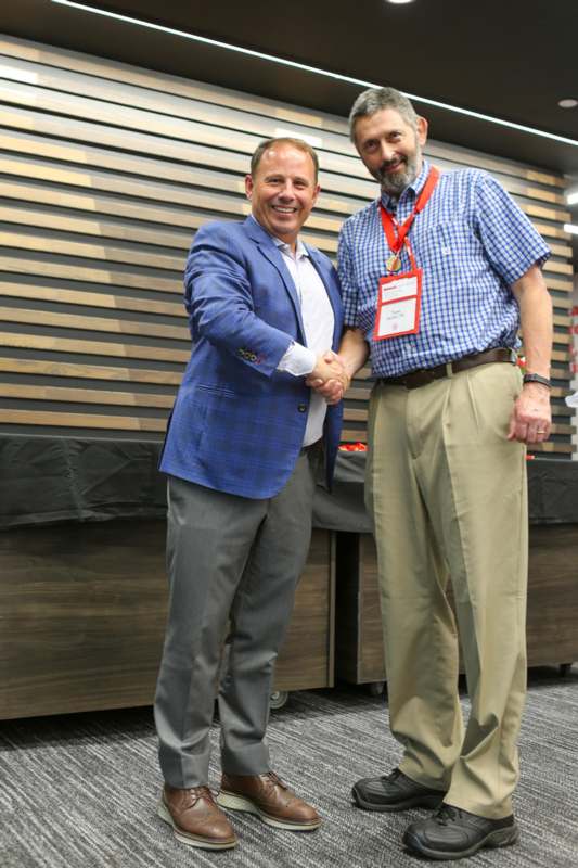 two men shaking hands in front of a wood wall