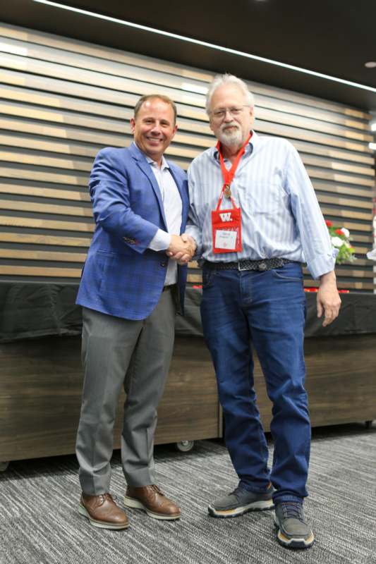 two men shaking hands in front of a wood wall