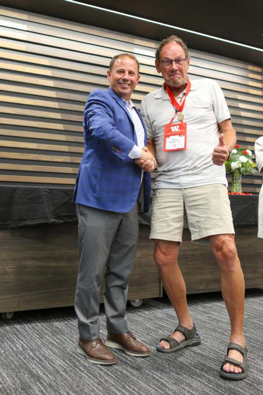 two men shaking hands in front of a wood wall