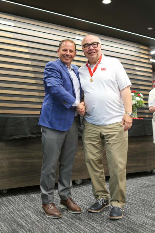 two men shaking hands in front of a wood wall