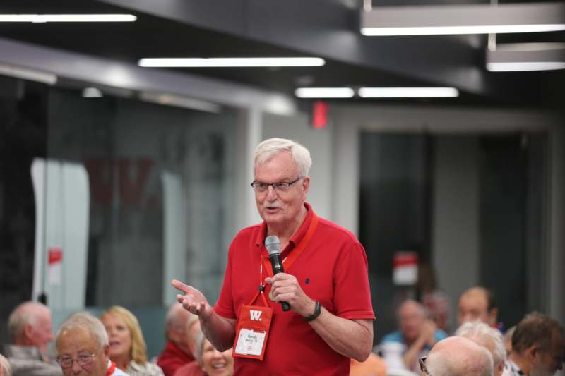 a man in a red shirt speaking into a microphone
