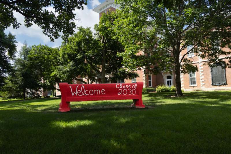 2026 New Student Move In - a red bench with white writing on it in front of a building