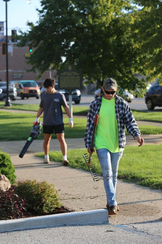 a man walking on a sidewalk with a rake and a man in a hat