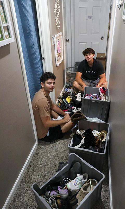 two men sitting on the floor with boxes full of shoes