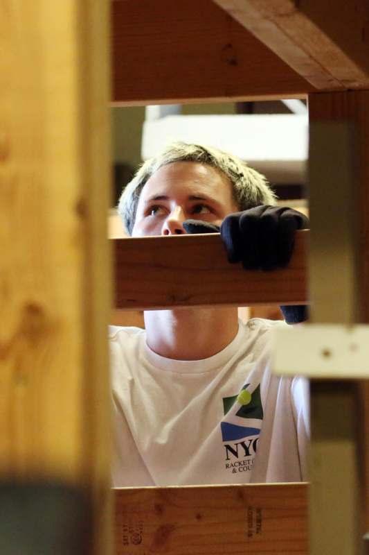 a man in a white shirt and black gloves holding a wooden beam