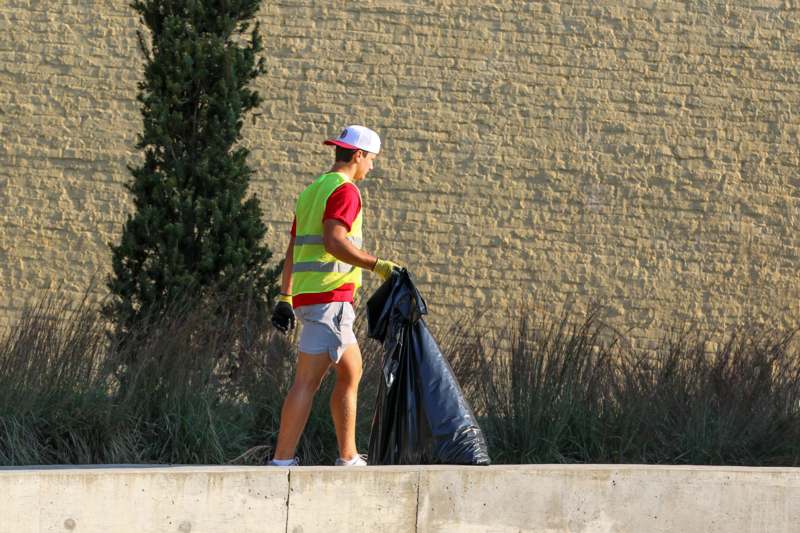 a man in a vest and gloves carrying a black bag