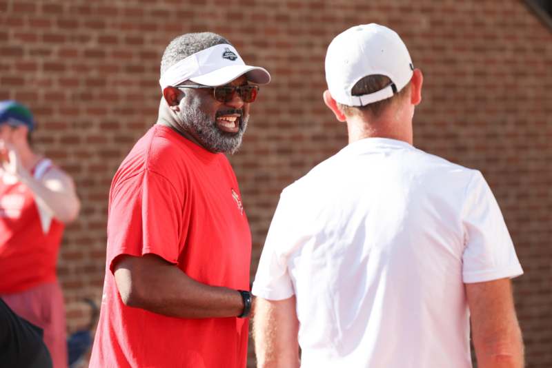 a man in a red shirt and white hat talking to another man