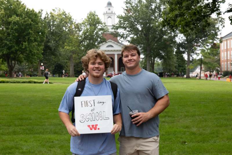 two men standing in a grassy area holding a sign