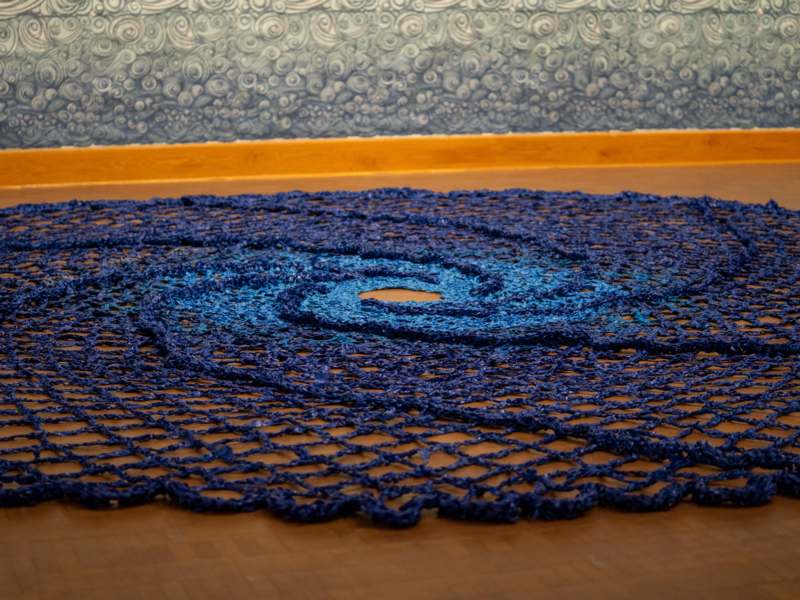 a blue crocheted rug on a wood floor