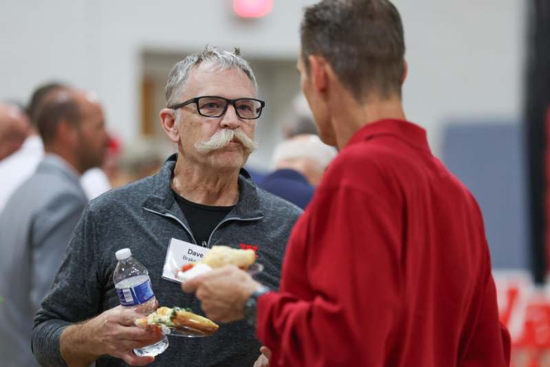 a man with a mustache and glasses holding food and a bottle of water