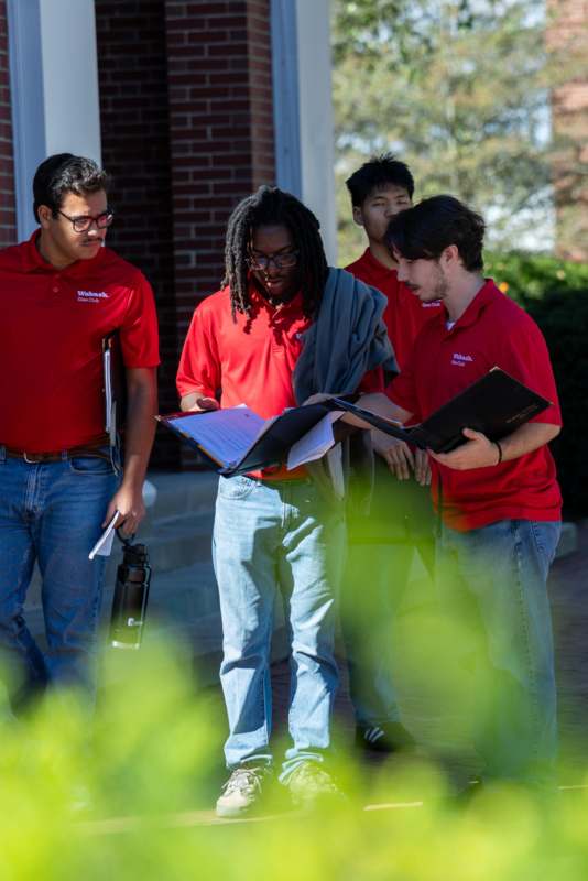 a group of men standing outside of a building looking at a folder