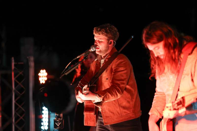 a man singing into a microphone with a guitar and a woman playing guitar