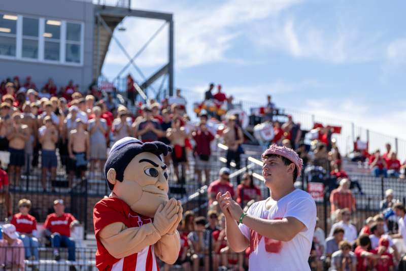 a man clapping hands with a mascot in front of a crowd