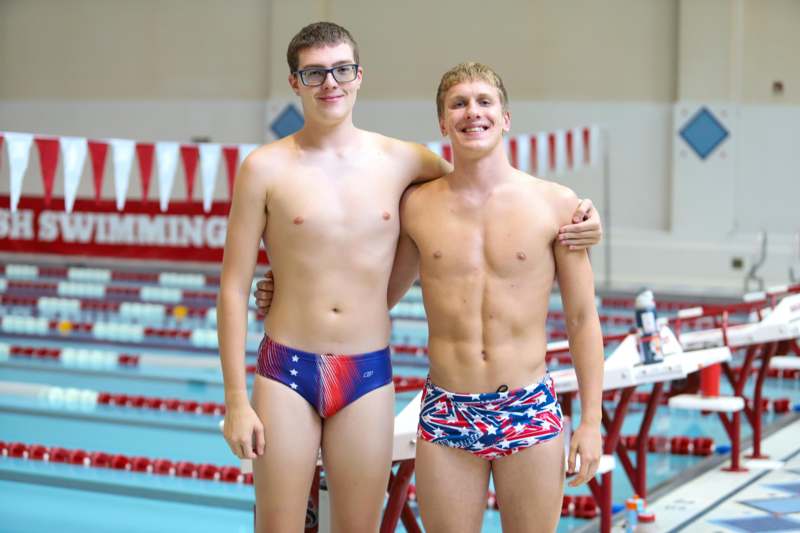 two men in swim trunks standing next to a pool