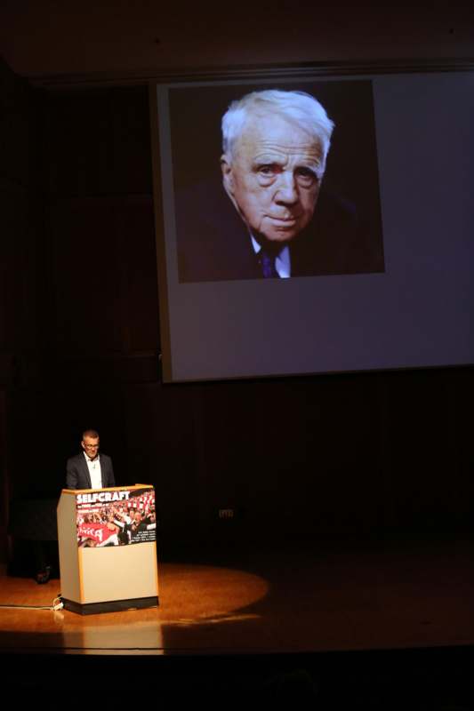 a man standing at a podium with a projector screen