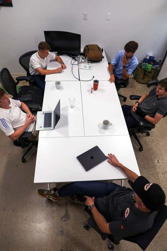 a group of men sitting around a table with laptops
