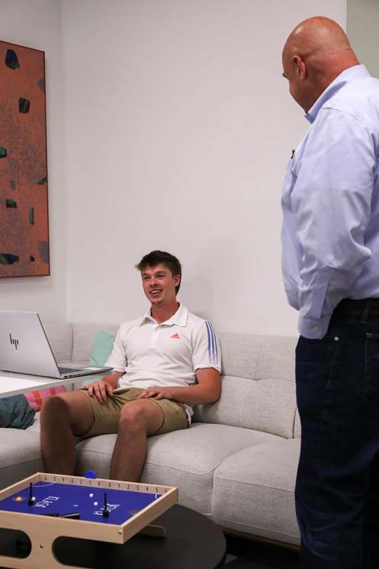 a man sitting on a couch with a laptop and a man looking at him