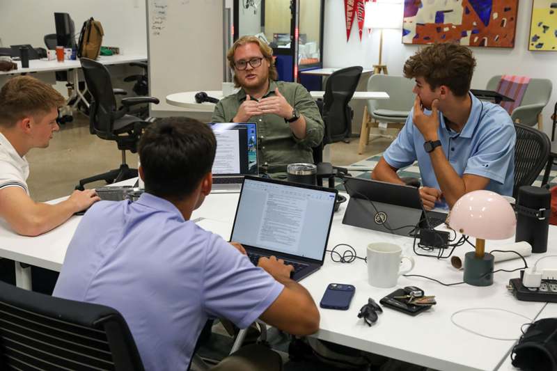a group of men sitting around a table with laptops