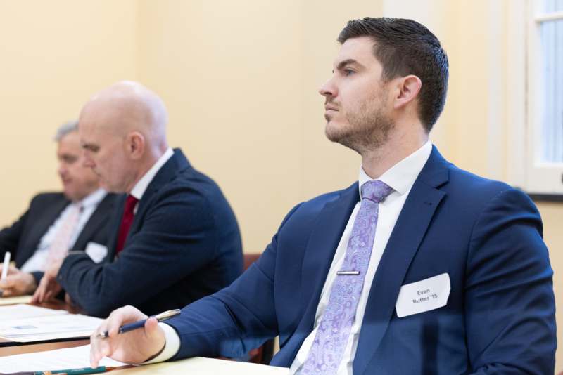 a man in a suit sitting at a table with other men in suits
