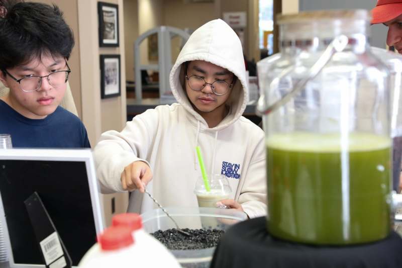 a man in a white hoodie holding a spoon in front of a container of green liquid